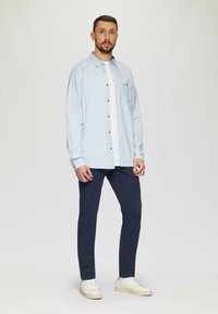 Hellblau kariertes Hemd mit langen Ärmeln, kombiniert mit dunkelblauen Hosen und weißen Sneakern. Klare Linien, Knopfverschluss, lässiger Stil.