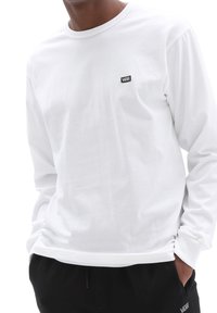 Langärmliges, weißes Baumwoll-T-Shirt mit einem Rundhalsausschnitt und einem kleinen schwarzen Vans-Logo-Patch auf der linken Brust.