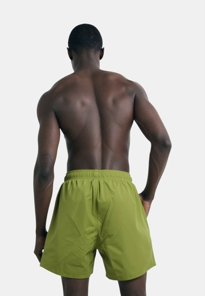 Shorts de bain verts avec une taille élastique, fabriqués en matériau léger, présentant une texture lisse et un design simple, vus de dos.