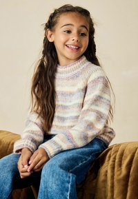 Monivärinen neulepaita, jossa on korkea kenttäkuvioitu kaulus, ja jossa on vaaleita raitoja kerma, sininen ja vaaleanpunainen. Paitaa on yhdistetty sinisiin farkkuihin.