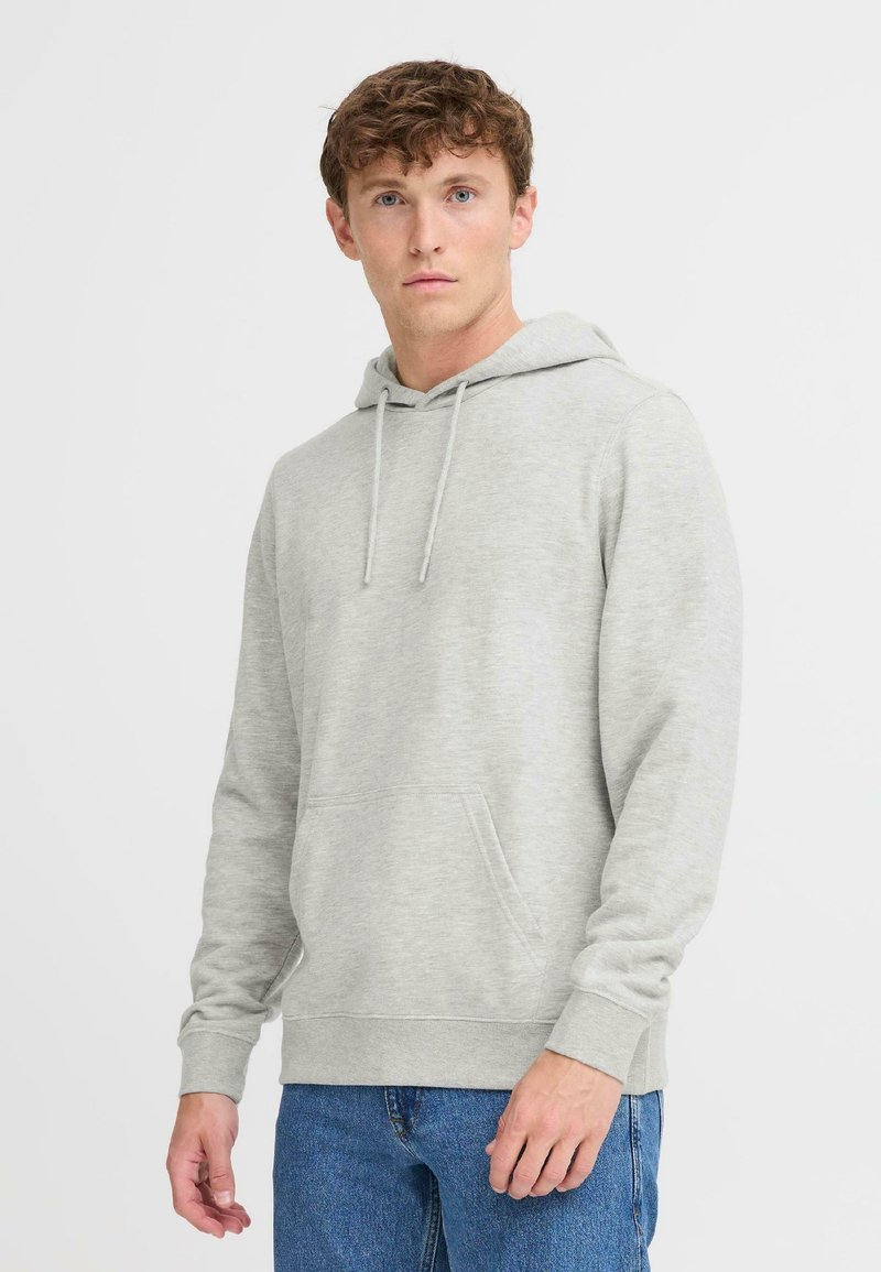 Sudadera gris claro hecha de un tejido suave, con un bolsillo frontal, capucha ajustable con cordón y puños acanalados. Combinada con pantalones vaqueros azules.