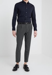 Marineblå skjorta med knappar, kombinerad med grå rutig byxa och svart bälte. Byxorna har en veckad front och avsmalnande ben, bärs med svarta skor.