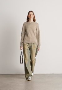 Beige textured sweater with a rounded neckline, paired with loose greenish-beige pants; person holding a silver bag.