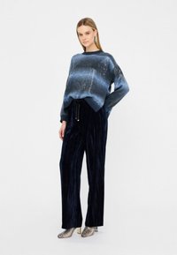 Maglione a righe blu e grigio lavorato a maglia con vestibilità morbida, abbinato a pantaloni a gamba larga in velluto blu navy e scarpe con tacco argentate metallizzate.