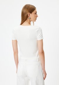 Hvid kortærmet t-shirt i blødt materiale, tætsiddende design, med rund halsudskæring og sømløse skuldre, parret med hvide højtaljede bukser.