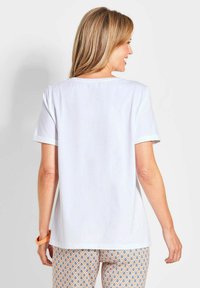 T-shirt blanc à manches courtes en tissu doux, avec un col rond et des poignets roulés. Associé à des leggings à motifs en bleu et orange.