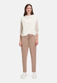 Luźna, kremowa bluzka z polaru z wysokim kołnierzem noszona na paskowanym długim rękawie, w połączeniu z miękkimi, taupe joggerami i białymi sneakersami.