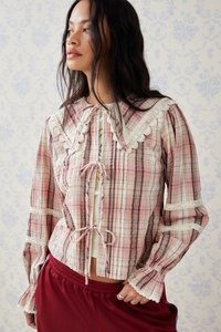 Blusa a quadri rosa con colletto bordato in pizzo, maniche lunghe e scollatura con cordoncino. Il tessuto ha una finitura testurizzata e un design leggero.
