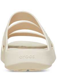 Białe klapki Crocs z płaską podeszwą, trzema szerokimi paskami górnymi i teksturowanym wnętrzem dla komfortu. Logo wytłoczone na pięcie.