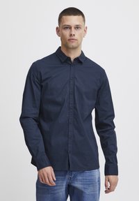 Camicia blu marina con bottoni realizzata in cotone, caratterizzata da un colletto classico, maniche lunghe e chiusura a bottoni, abbinata a jeans azzurri chiari.
