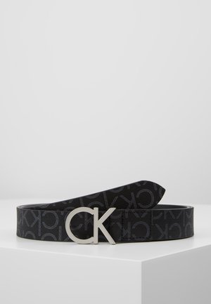 Ceinture de créateur noire avec motif répété "CK" et boucle logo argentée "CK" reposant sur une surface blanche.