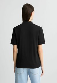 Zwarte poloshirt met een kort, opgerold mouwontwerp en een klassieke kraag. Gemaakt van soepel stof, met een rechte zoom en minimale details.