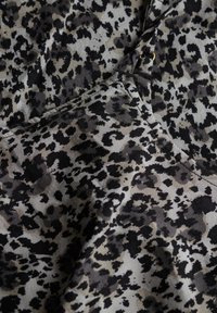 Leopardprintstof i nuancer af grå og sort med blød tekstur; indeholder subtile variationer i mønsteret og en lille gulddetalje.