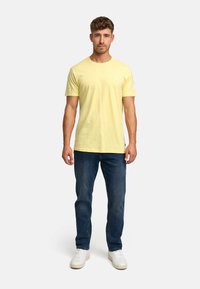T-shirt à manches courtes jaune en coton doux, associé à un jean bleu foncé et des baskets blanches. Encolure ronde simple, coupe décontractée.