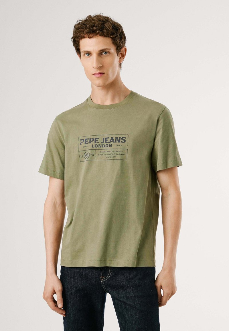Olive zaļš kokvilnas T-krekls ar īsām piedurknēm un noapaļotu apkakli. Priekšpusē ir grafika ar tekstu "PEPE JEANS LONDON" un papildu tekstu.