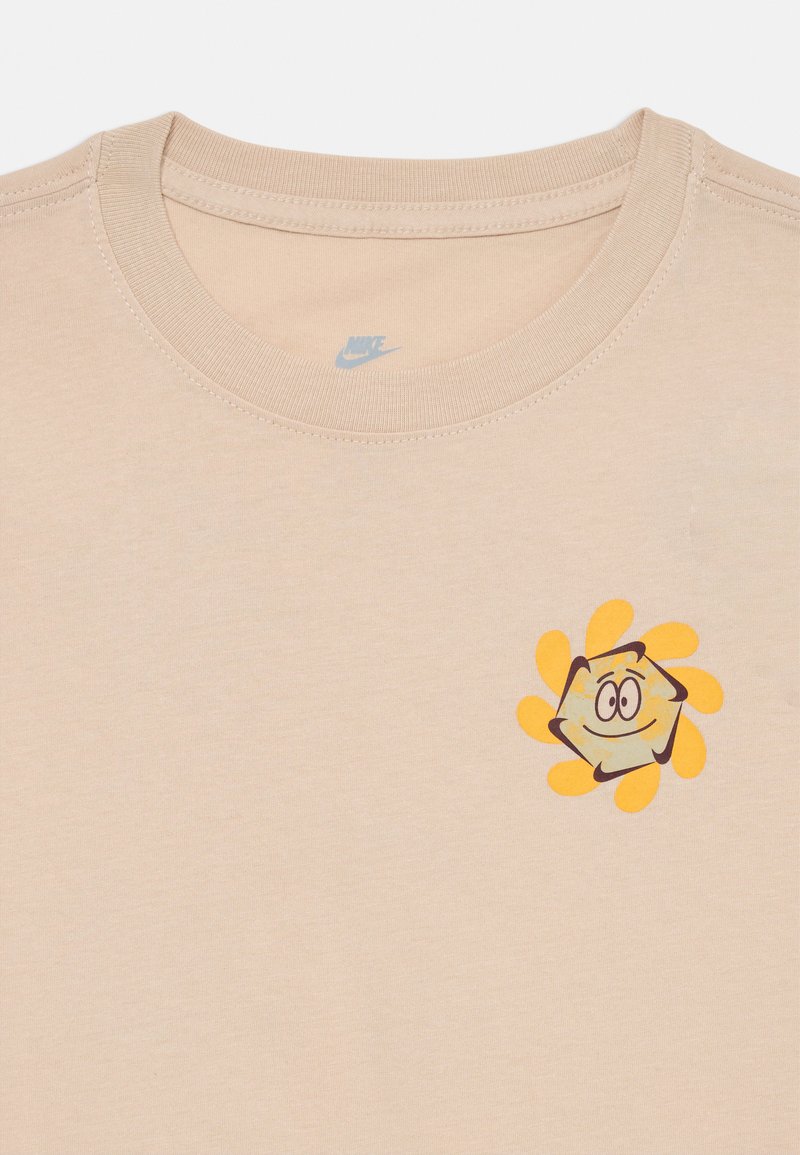 T-shirt en coton beige avec un col rond, arborant un graphique d'un soleil en cartoon jaune avec un visage souriant et des rayons orange.