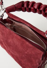 Burgundy suede handbag with a braided leather handle and silver zipper. Interior features a smooth lining and a zippered pocket.