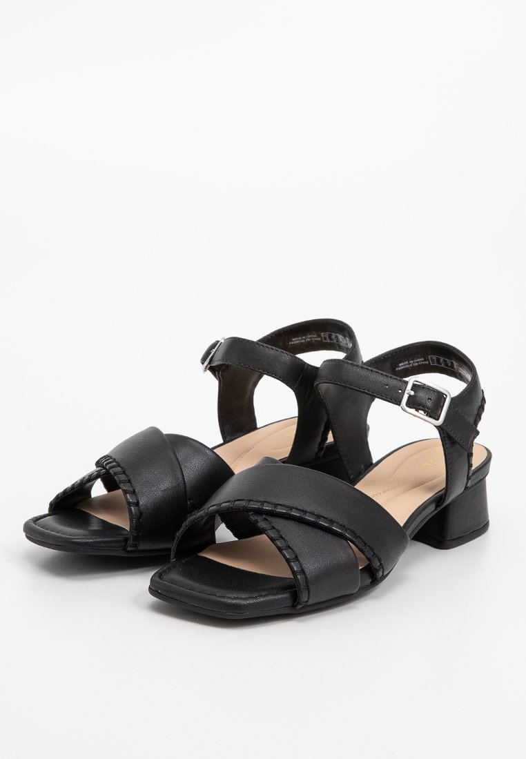 Sandalias de piel negra con tacón cuadrado, con correas entrelazadas y un detalle trenzado a lo largo de los bordes. Incluye una correa ajustable en el tobillo.