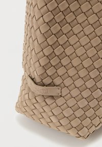 Πλεκτή τσάντα ώμου σε μπεζ χρώμα με ανάγλυφη εξωτερική επιφάνεια, διαθέτει ορθογώνιο σχήμα και λεπτομέρεια με ανάγλυφη ετικέτα. Ανθεκτικό υλικό με εκλεπτυσμένο σχεδιασμό.