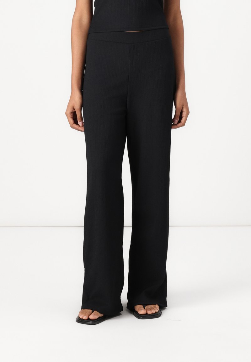 Black ribbed wide-leg pants feature a stretchy waistband and soft fabric, providing comfort and a relaxed fit. Floor-length design with minimal detailing.