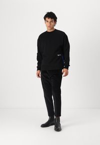 Hanorac negru cu guler rotund, croială lejeră și detaliu discret cu logo. Asortat cu pantaloni negri, îngustați și cizme negre până la glezne.