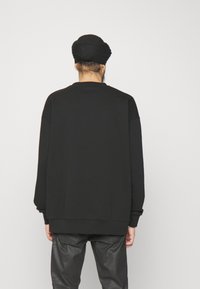 Sudadera negra de gran tamaño con mangas largas, cuello redondo y puños acanalados, combinada con pantalones negros. Textura de tela suave.
