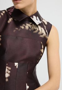 Ärmelloses Kleid aus strukturiertem Stoff, mit einem dunkelroten Grundton und hellen abstrakten Mustern sowie einem klassischen spitzen Kragen.