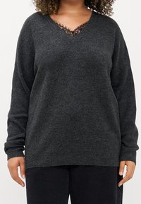 Mörkgrå tröja med V-ringning som har svart spetskant vid halsringningen. Långa ärmar med ribbade mudd, mjuk textur, avslappnad passform.