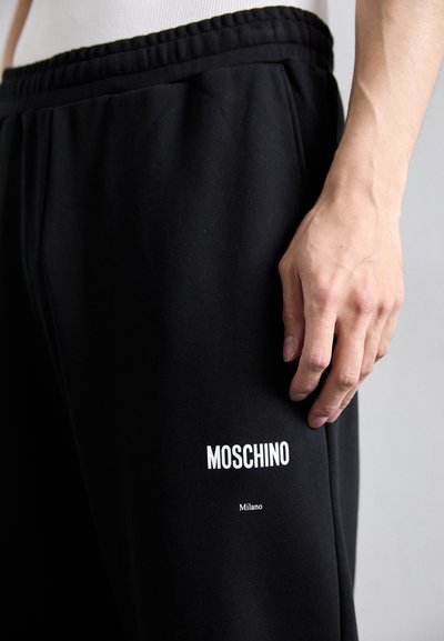 Svarta joggerbyxor i mjukt tyg, med elastisk midja och vit "Moschino" märkning på vänster ben.