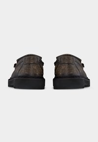 Καφέ δερμάτινα παπούτσια AllSaints London, εμφανιζόμενα από πίσω, με χοντρές μαύρες σόλες σε λευκό φόντο.