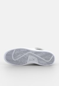 Semelle de chaussure de sport noire et blanche avec un motif de chevrons, présentant un logo visible et un matériau en caoutchouc lisse.