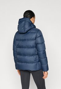 Marineblå dunjakke med hætte, der har quiltede sektioner og en glat, skinnende overflade. Designet til at holde varmen med en afslappet pasform.