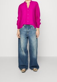 Fuchsia button-up blouse van textiel met een gestructureerde stof, wijde mouwen en een v-hals. Gekenmerkt met versleten, oversized blauwe denim jeans en metallic schoenen.