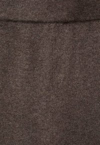 Ruskea neulottu kangas, jossa on pehmeä tekstuuri ja hieman poimuttunut muotoilu. Pinta on tasainen ja säännöllisesti jaoteltu kuvio.