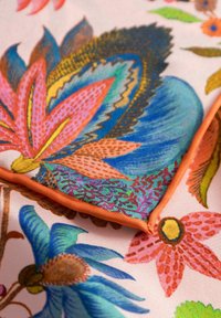 Kleurrijke stof met een bloemenpatroon in levendig roze, blauw en groen, omzoomd met oranje bies, met complexe details en textuur.