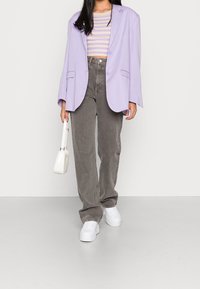 Lavender oversized blazer, striped cropped top, gray high-waisted jeans, white sneakers, and a small white handbag. Textured fabric details visible.