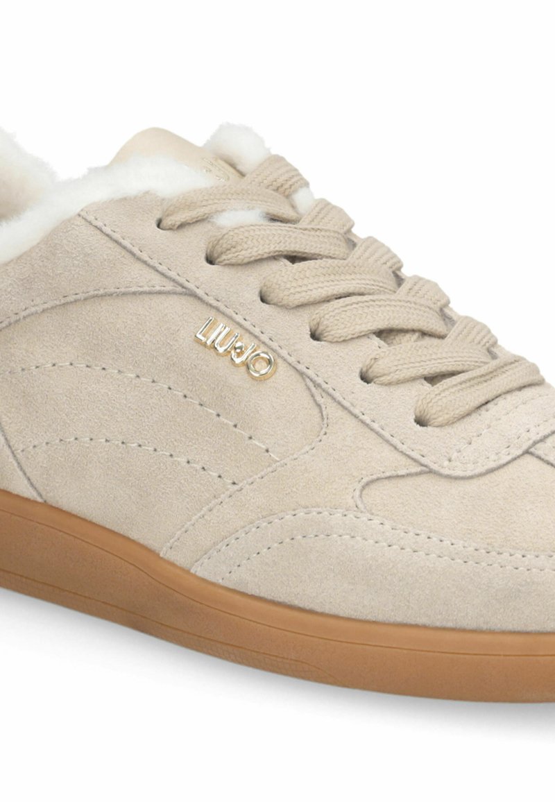 Beige Wildlederschuh mit Gummisohle, runder Zehenpartie und weichem Innenfutter, verziert mit tonal abgestimmten Nähten und einem kleinen goldenen Logo.