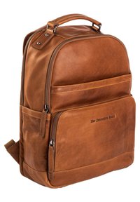 Mochila de cuero marrón con una textura suave, que cuenta con un asa superior, compartimentos con cremallera y un discreto logotipo en la parte frontal.