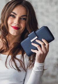 Navy leather wallet with a textured flap closure, silver accent, and stitching details, held in a hand against a light background.