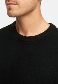 Musta neulepusero, jossa on ribbikuvioitu pyöreäkaula. Kangas näyttää pehmeältä ja teksturoidulta, ja siinä on vain vähäisiä yksityiskohtia tai kuvioita.