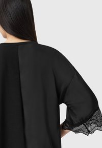 Sort satin top med en afslappet pasform, blondedetalje p�å ærmerne og en glat tekstur. Bagviewet fremhæver det elegante design.