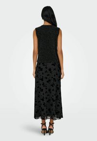 Czarny bezrękawnik z teksturowanym wzorem, w zestawieniu z lejącą się czarną spódnicą zdobioną kwiatowymi motywami. Całość dopełniają czarne sandały na wysokim obcasie.
