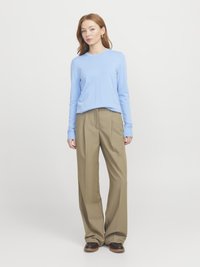 Helles blaues Langarmshirt, kombiniert mit beigen, weit geschnittenen Hosen. Das Shirt hat einen runden Hals und die Hosen haben eine glatte, maßgeschneiderte Verarbeitung.