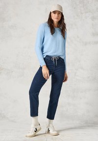 Ljusblå långärmad topp med ribbstruktur, mörkblå randiga byxor, vita sneakers och en beige keps. Avslappnad, bekväm outfit.