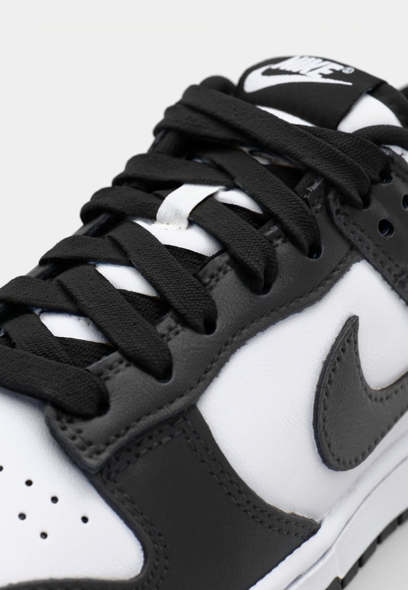 Schwarz-weißer Sneaker mit einem Obermaterial aus Leder, ausgestattet mit einem auffälligen Swoosh-Logo, strukturierten Schnürsenkeln und Belüftungsöffnungen an der Zehenbox.