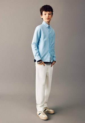 Chemise boutonnée bleu clair avec col, pantalon blanc droit, et baskets claires. Design minimaliste, texture lisse, et style décontracté.