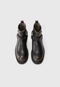 Botas de tobillo de cuero negro con un acabado suave, dos hebillas metálicas y una suela texturizada. Corte bajo con un talón reforzado.