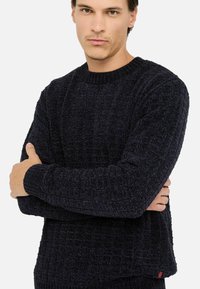 Maglione lavorato a maglia blu navy con un motivo testurizzato, collo a girocollo a coste e polsini. Presenta un piccolo accento rosso all'orlo.