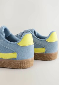 Blaue Wildleder-Sneaker mit gelben Akzenten und einer strukturierten braunen Gummisohle. Das Design umfasst einen gepolsterten Schaft und Zunge.