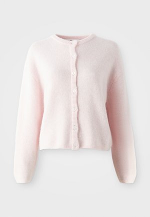Ljusrosa, kort cardigan i mjukt, fluffigt tyg. Har en rund halsringning och åtta vita knappknäppningar framtill.